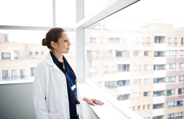 Junior doctor in white coat looking through hospitalwindow